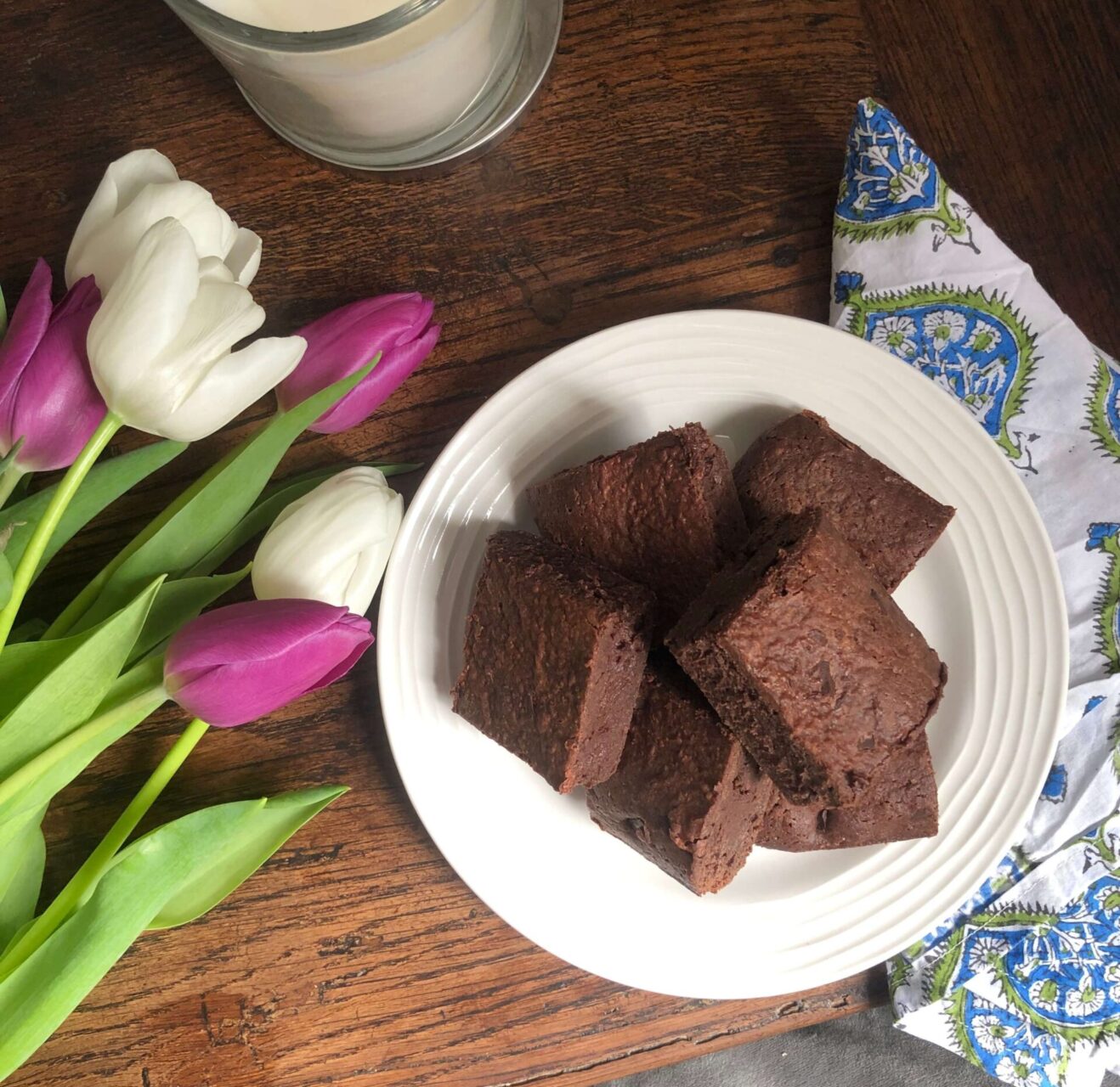 A plate of brownies on a white plate next to some white and purple tulips. All the brownies are soon to be eaten by copywriter Bonnie Harrington with a massive cuppa.