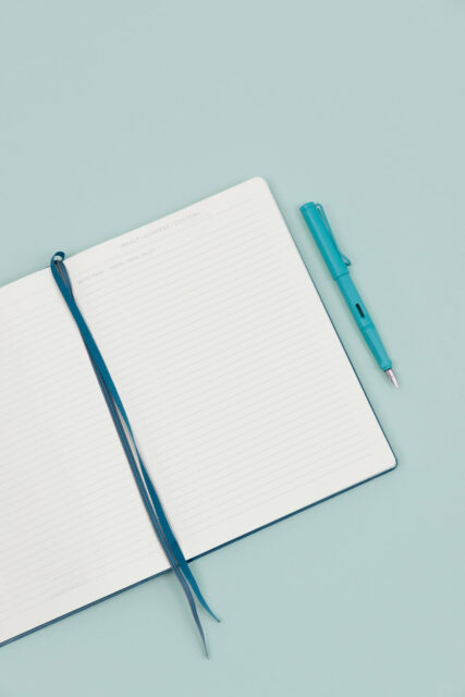 An open notebook with a turquoise fountain pen to the side