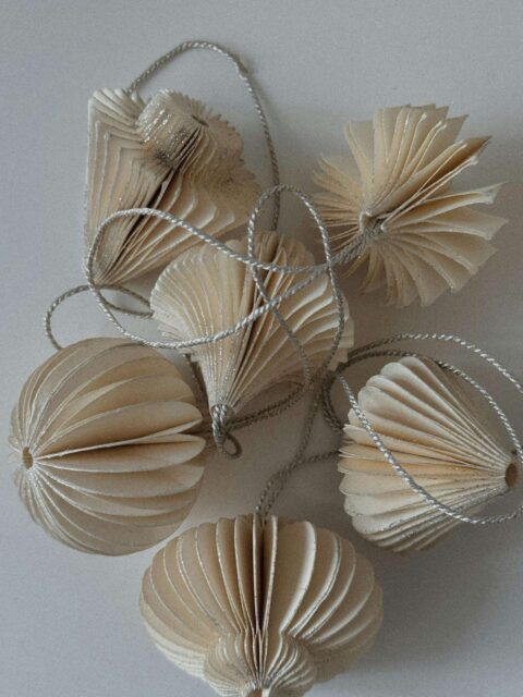 A close up from above of paper christmas baubles. White background, creamy paper baubles, silver strings. Christmassy but not super colourful/ jazzy/ intense Christmas vibes
